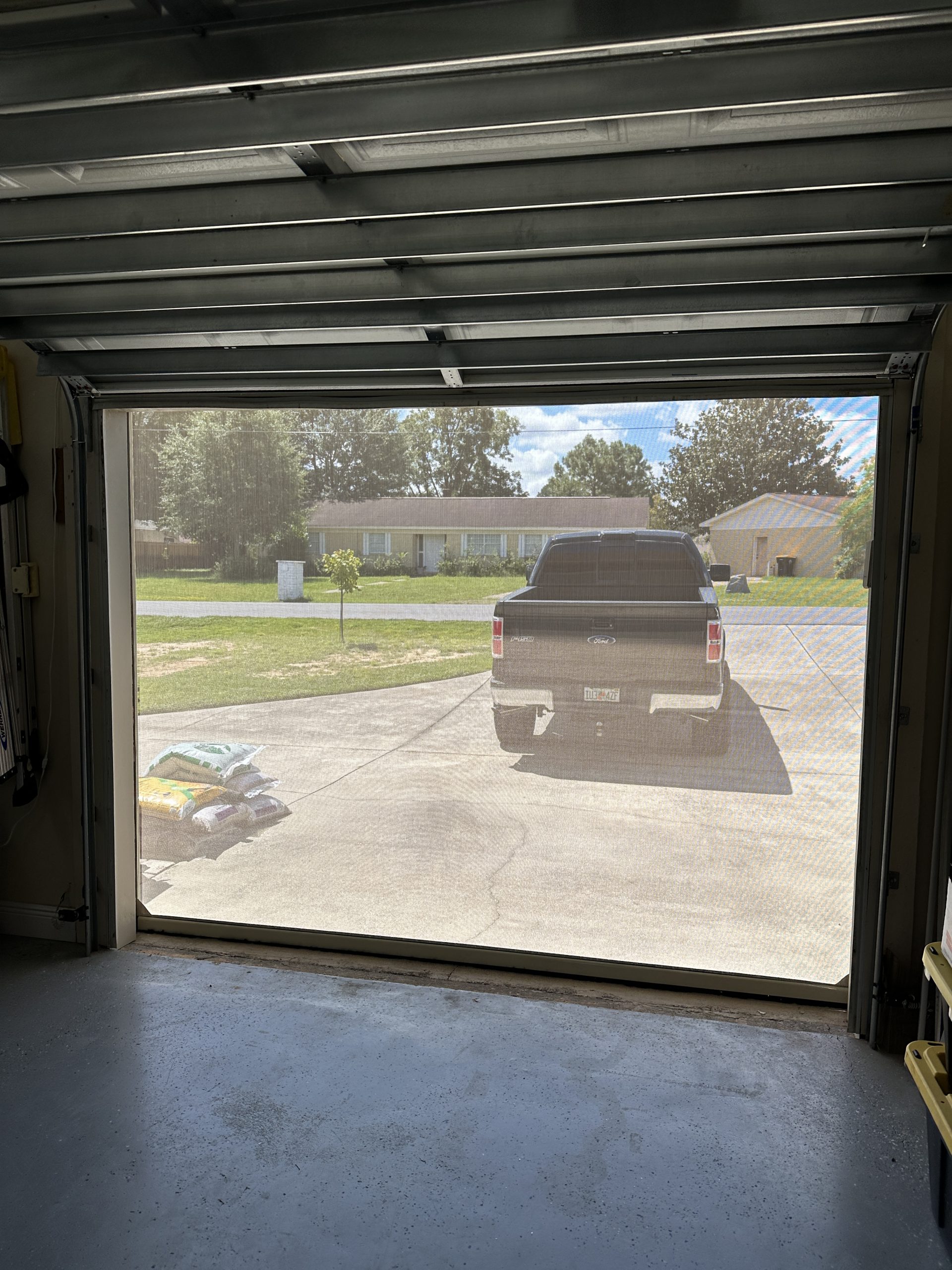 View from inside garage through motorized retractable screen showing outdoor visibility, airflow, and light filtration