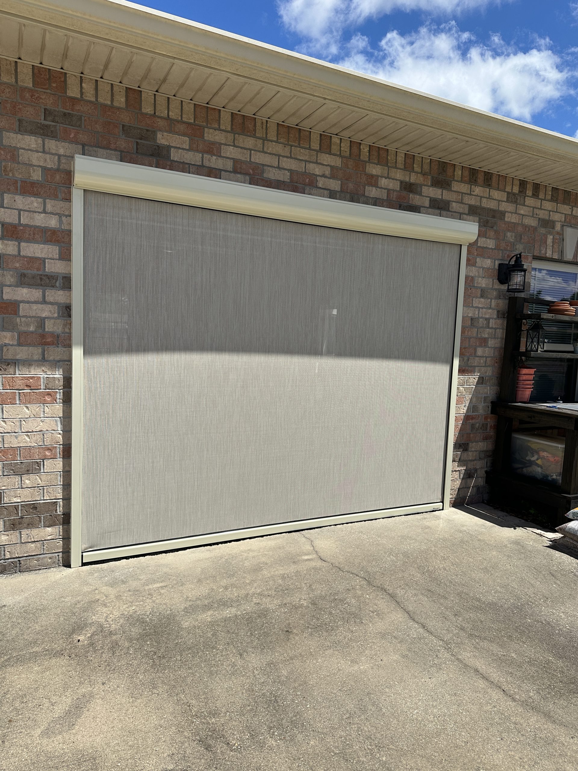 Motorized retractable screen installed on residential garage providing shade, airflow, and insect protection.